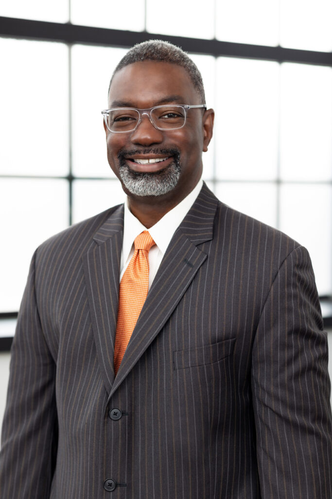 in studio professional headshot of a man in a gray striped suit with an orange tie