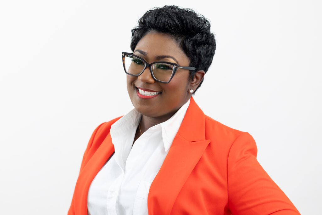 black lady with glasses taking a headshot photo in a orange suit
