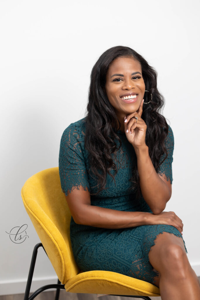 detroit professional headshots of a woman in a teal dress and yellow chair with a beautiful smile. image taken to update her website and social profiles